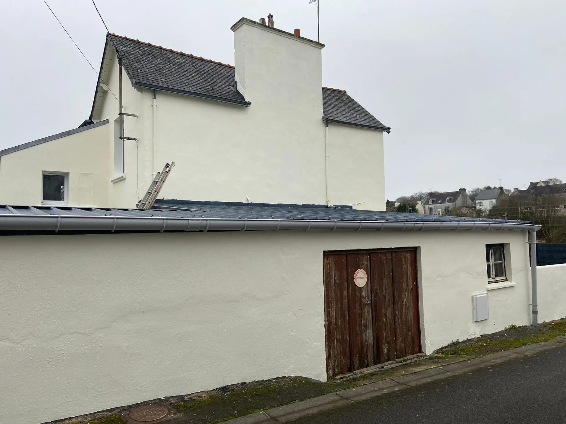 Annexe enduite bordée d'une gouttière sur toute sa longueur, descente d'eau à l'angle, échelle posée sur la couverture