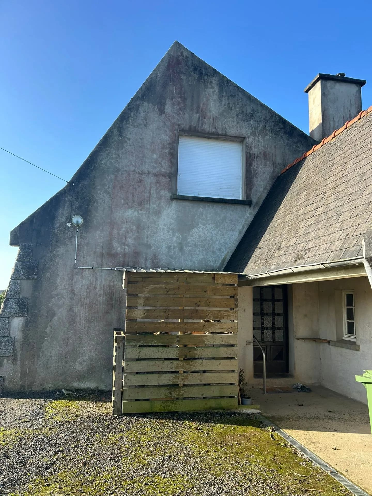 Mur pignon enduit, noirci et strié par les intempéries, sous une couverture en ardoise