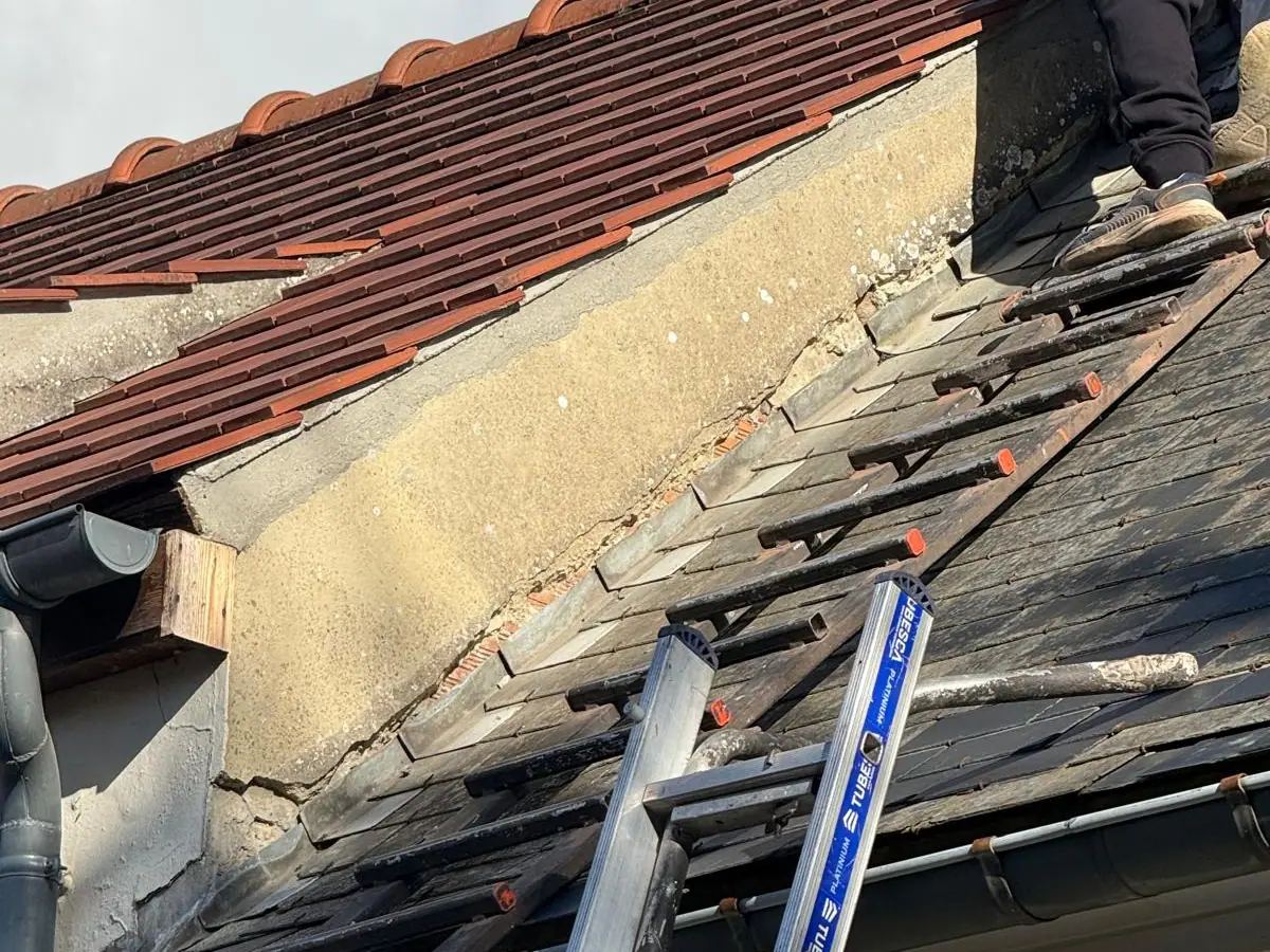Solin fissuré le long du mur, couvreur sur une échelle de toit posée sur les ardoises